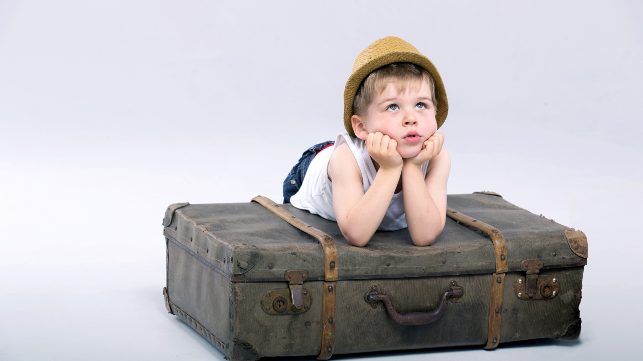 Маленький мальчик лежит на большом чемодане на сером фоне