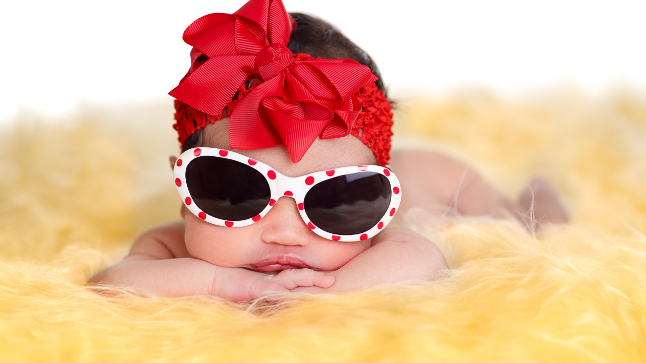 Маленькая забавная малышка в очках и с красным бантом на голове