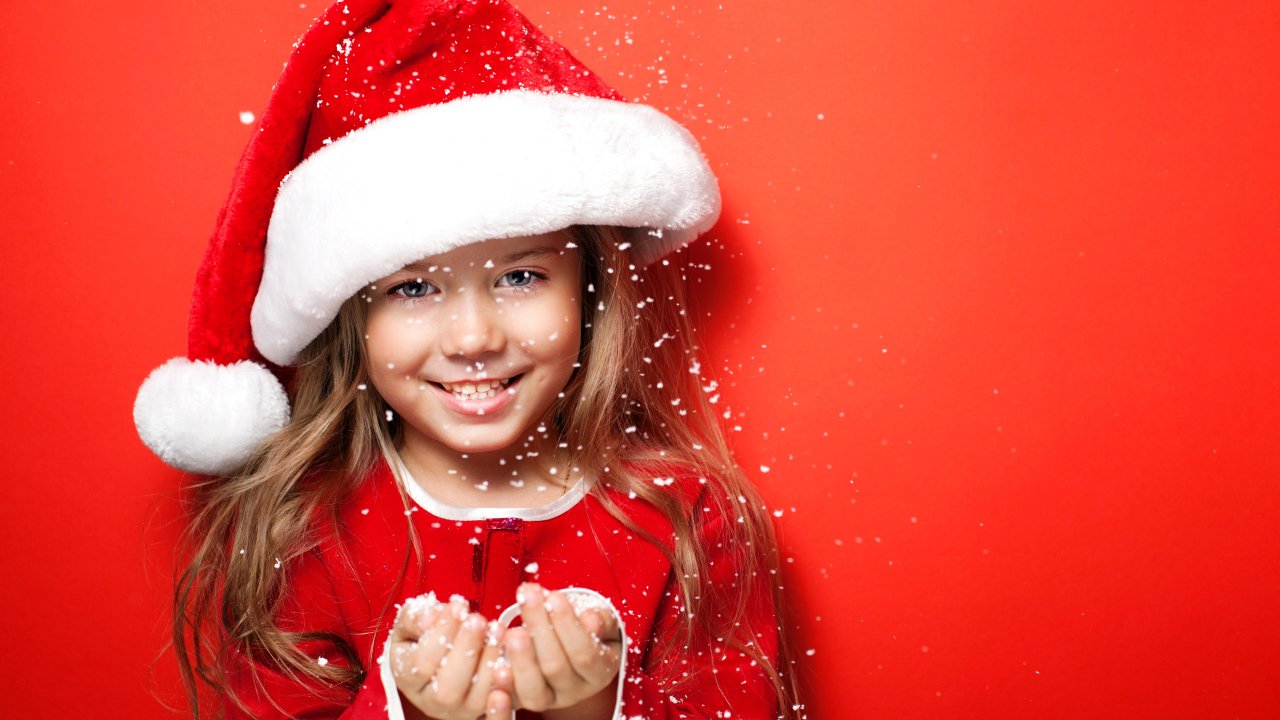 Маленькая девочка в новогодней шапке ловит руками снежинки