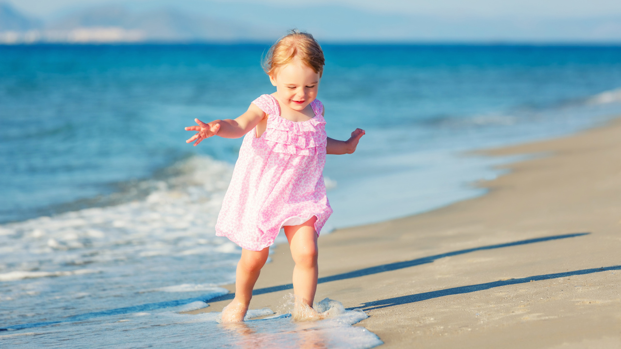 Маленькая девочка в розовом платье гуляет по морскому песку
