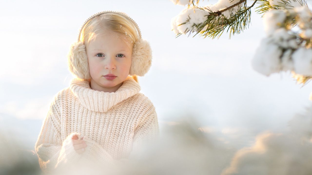 Маленькая девочка в белом свитере у покрытой снегом ели