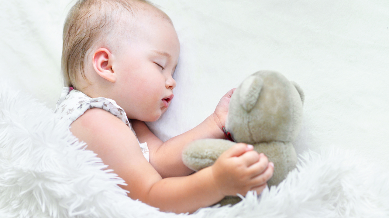 Маленькая девочка спит с мягкой игрушкой под белым одеялом