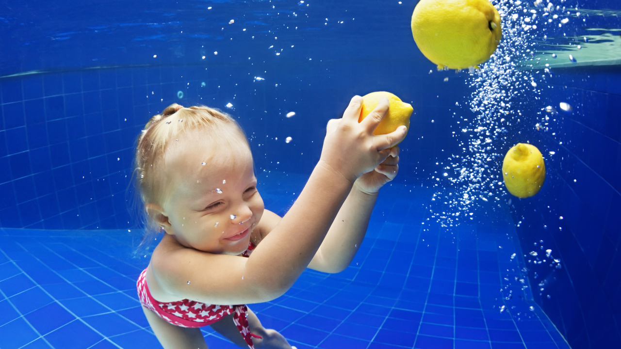 Маленькая девочка плавает в бассейне с желтыми лимонами