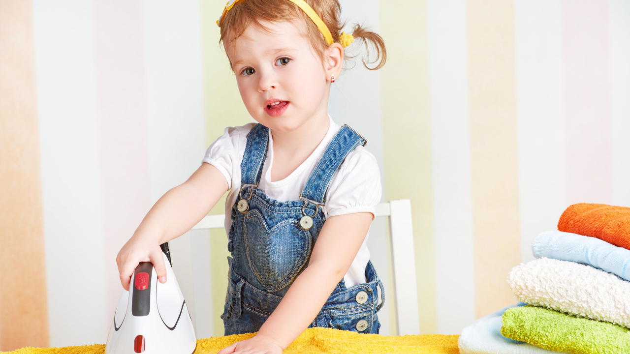 Маленькая девочка с утюгом гладит полотенце