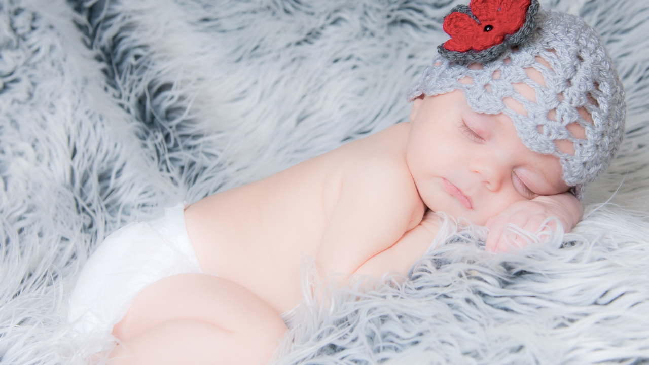 Спящий грудной ребенок в вязаной шапке с красным цветком на голове
