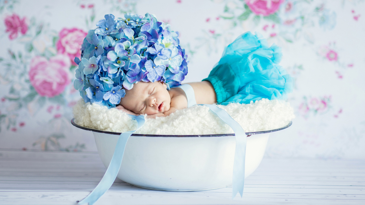 Маленький грудной ребенок спит в миске с шапкой из цветов гортензии на голове