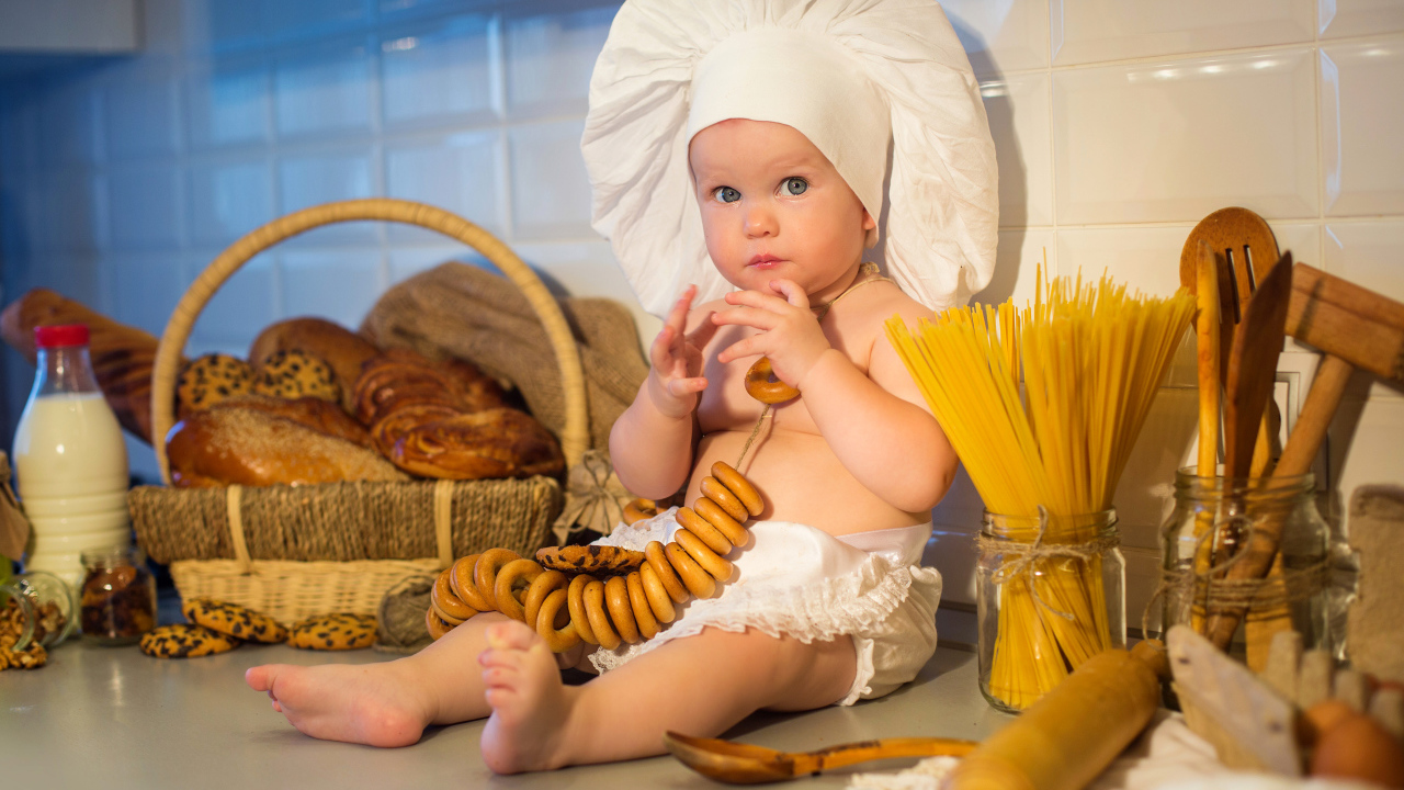 Маленький ребенок в шапке повара сидит на столе с выпечкой