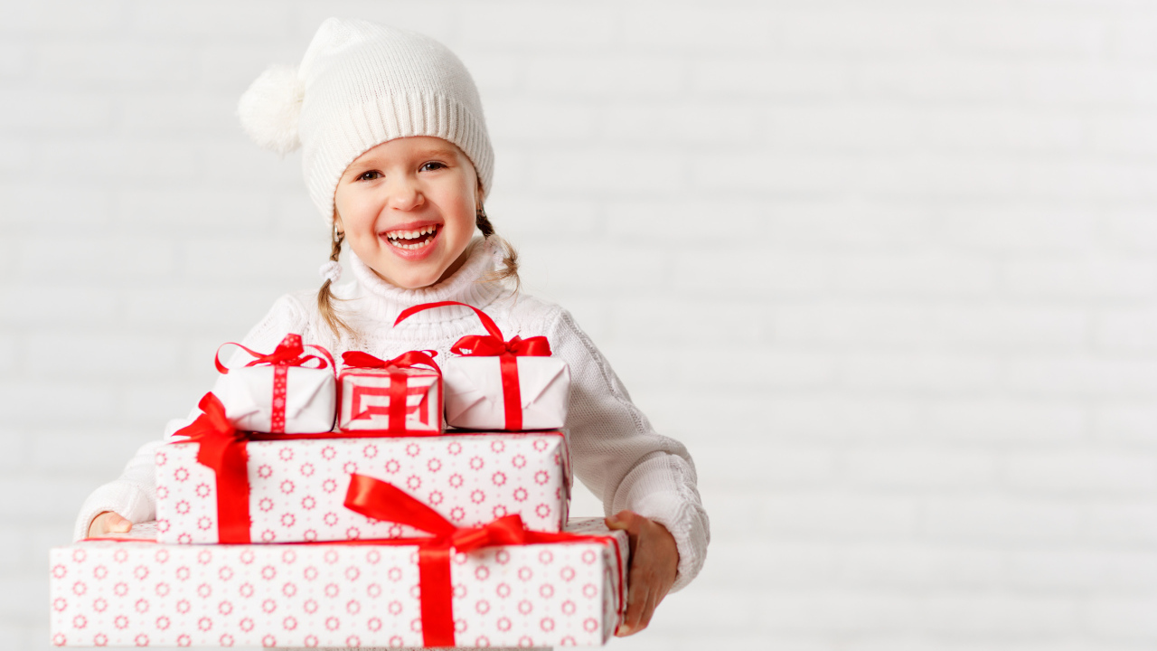 Смеющаяся девочка в белой шапке с новогодними подарками