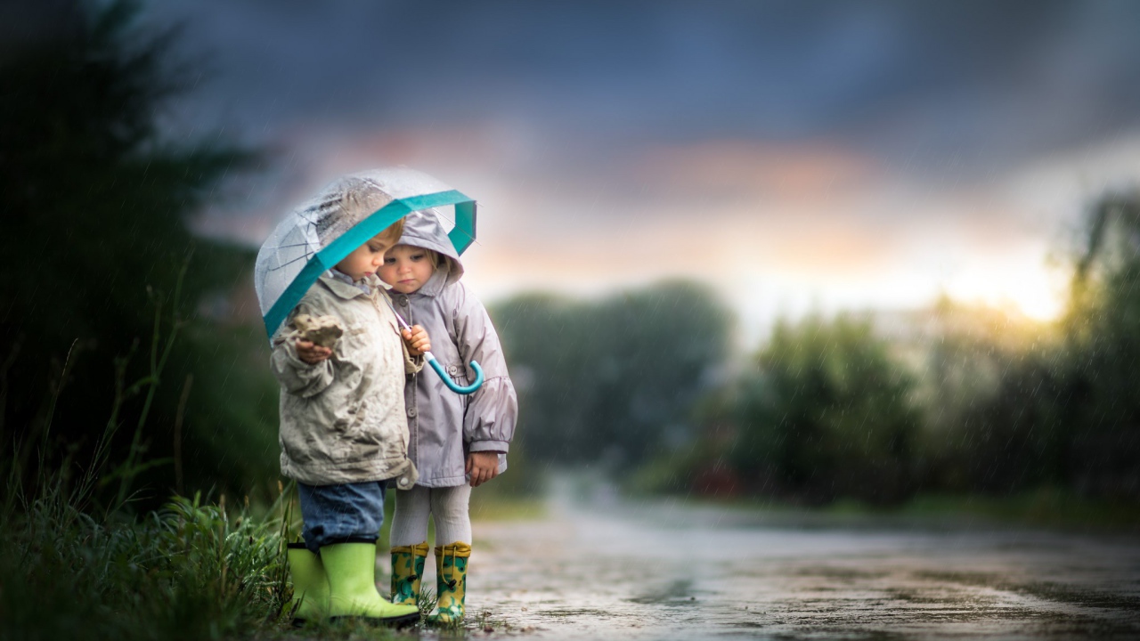 Маленькие мальчик и девочка под зонтом на дороге 