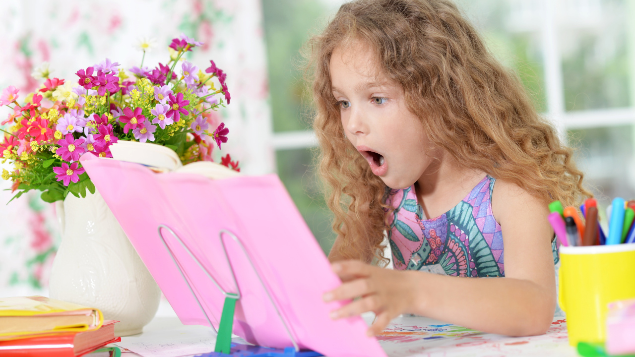 Маленькая русоволосая девочка удивленно смотрит в книгу