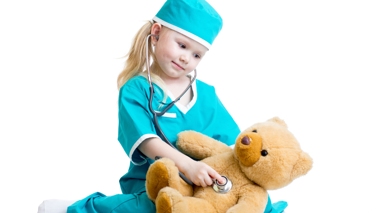 Маленькая девочка в костюме врача лечит плюшевого медвежонка