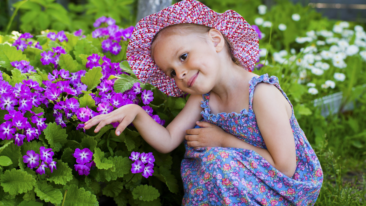 Маленькая девочка в шляпе рядом с фиолетовыми цветами