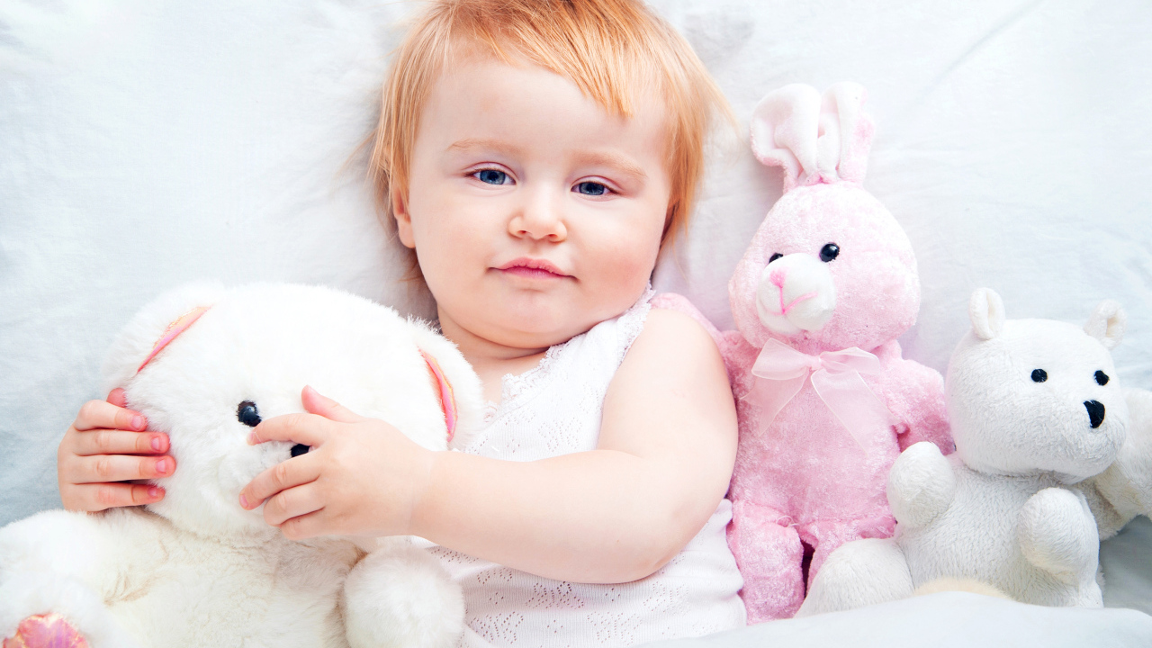 Маленькая девочка лежит в кровати с плюшевыми игрушками