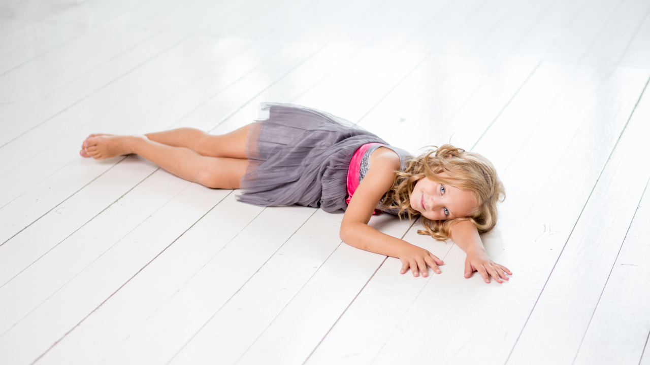Маленькая девочка модель в сером платье лежит на деревянном полу