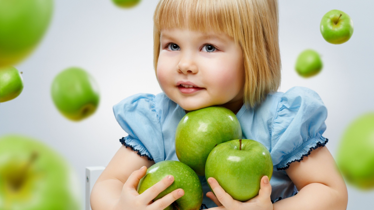 Маленькая девочка с зелеными яблоками в руках