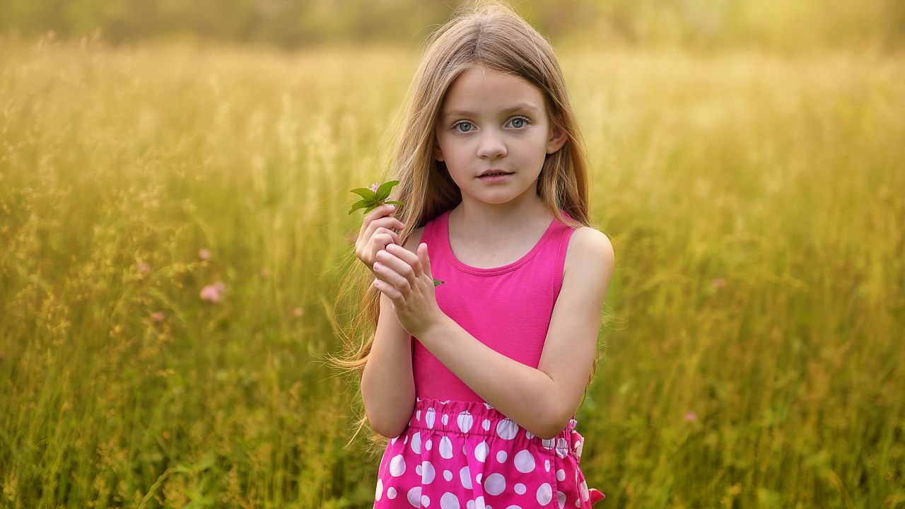 Маленькая длинноволосая девочка в розовом сарафане на поле