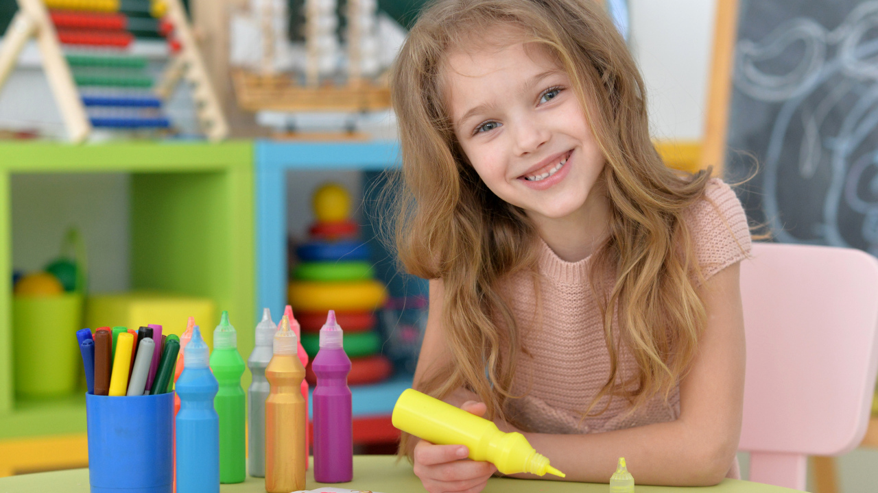 Маленькая улыбающаяся девочка рисует карандашами