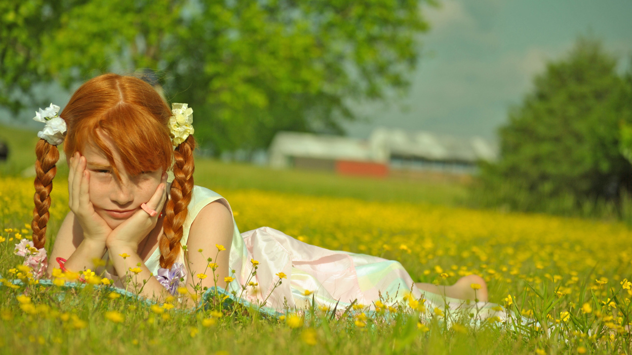 Рыжеволосая девочка с косичками лежит на зеленой траве