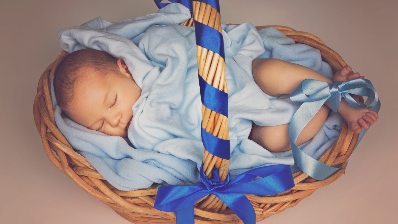 Спящий грудной ребенок в корзине с синими лентами