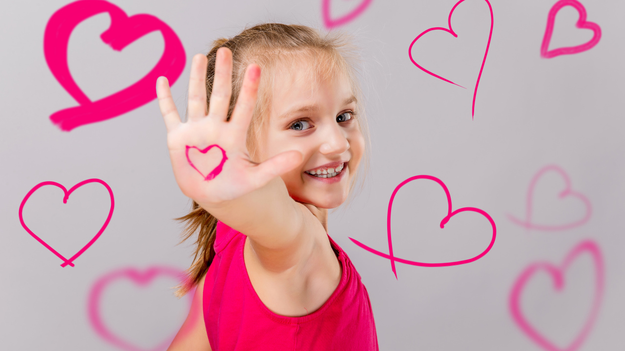Улыбающаяся девочка с нарисованными сердечками на сером фоне