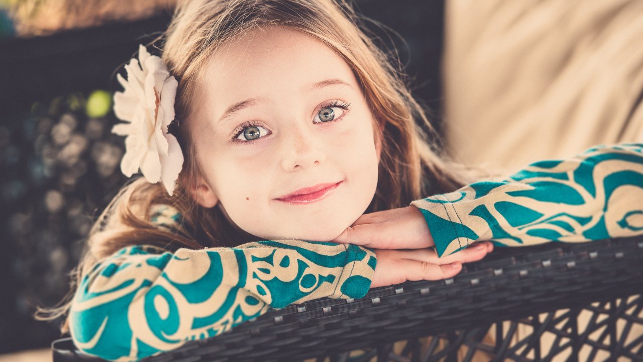 Улыбающаяся зеленоглазая девочка с белым цветком в волосах