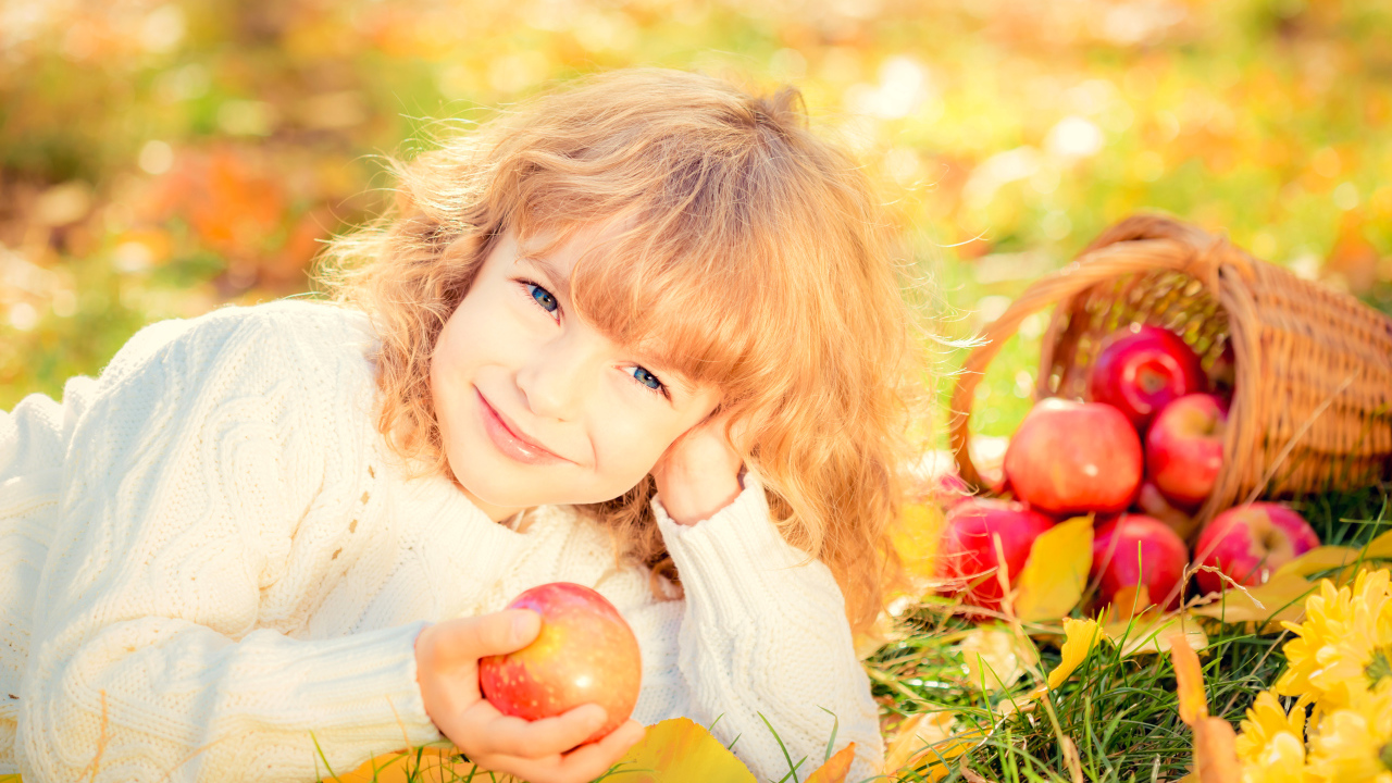 Улыбающаяся рыжеволосая девочка с корзиной красных яблок