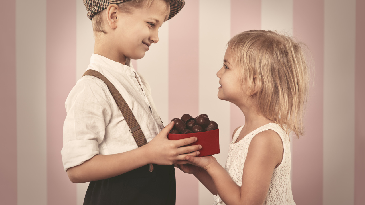 Мальчик дарит девочке коробку шоколадных конфет