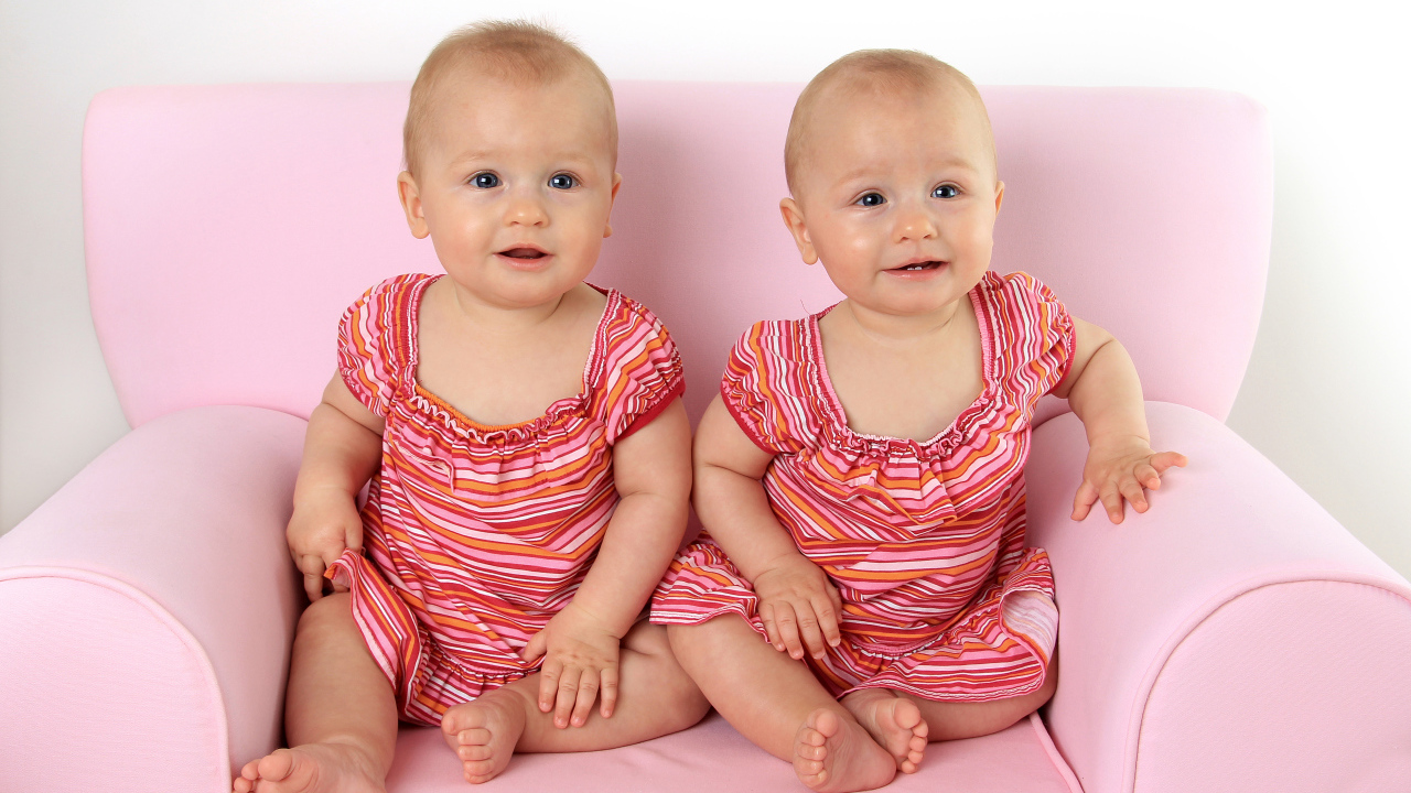 Две милые маленькие девочки сидят на розовом диване