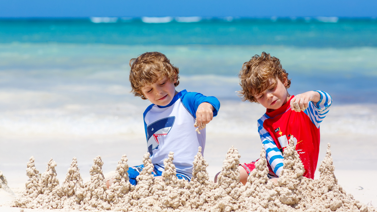 Два маленьких мальчика играют с песком на пляже