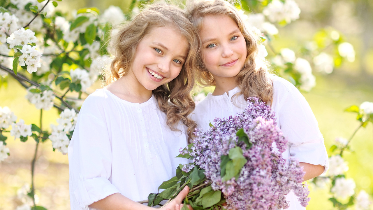 Две улыбающиеся девочки близняшки с букетом сирени