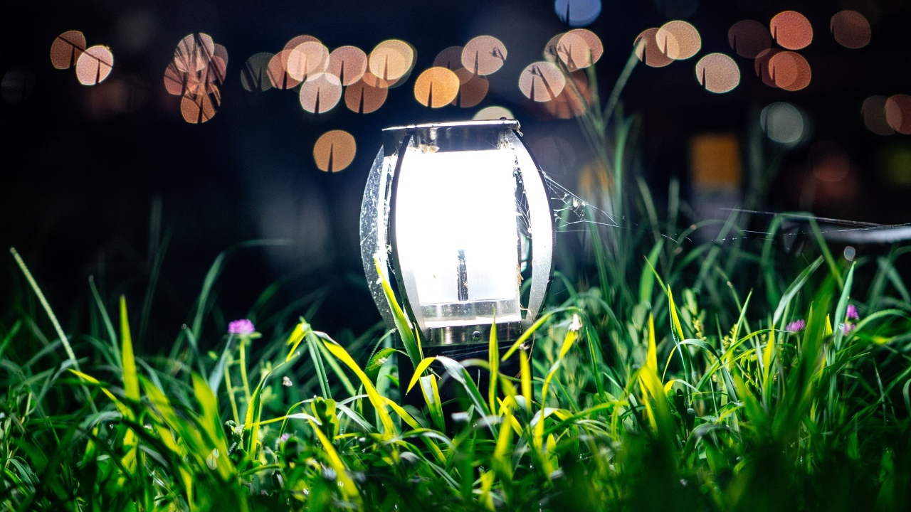 Включенный фонарь стоит в зеленой траве