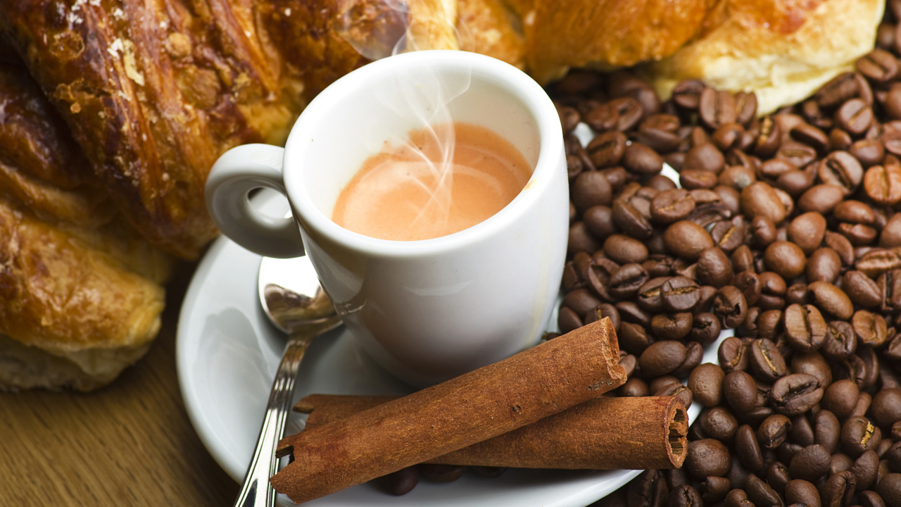 Чашка с горячим кофе на столе с корицей, зернами кофе и выпечкой