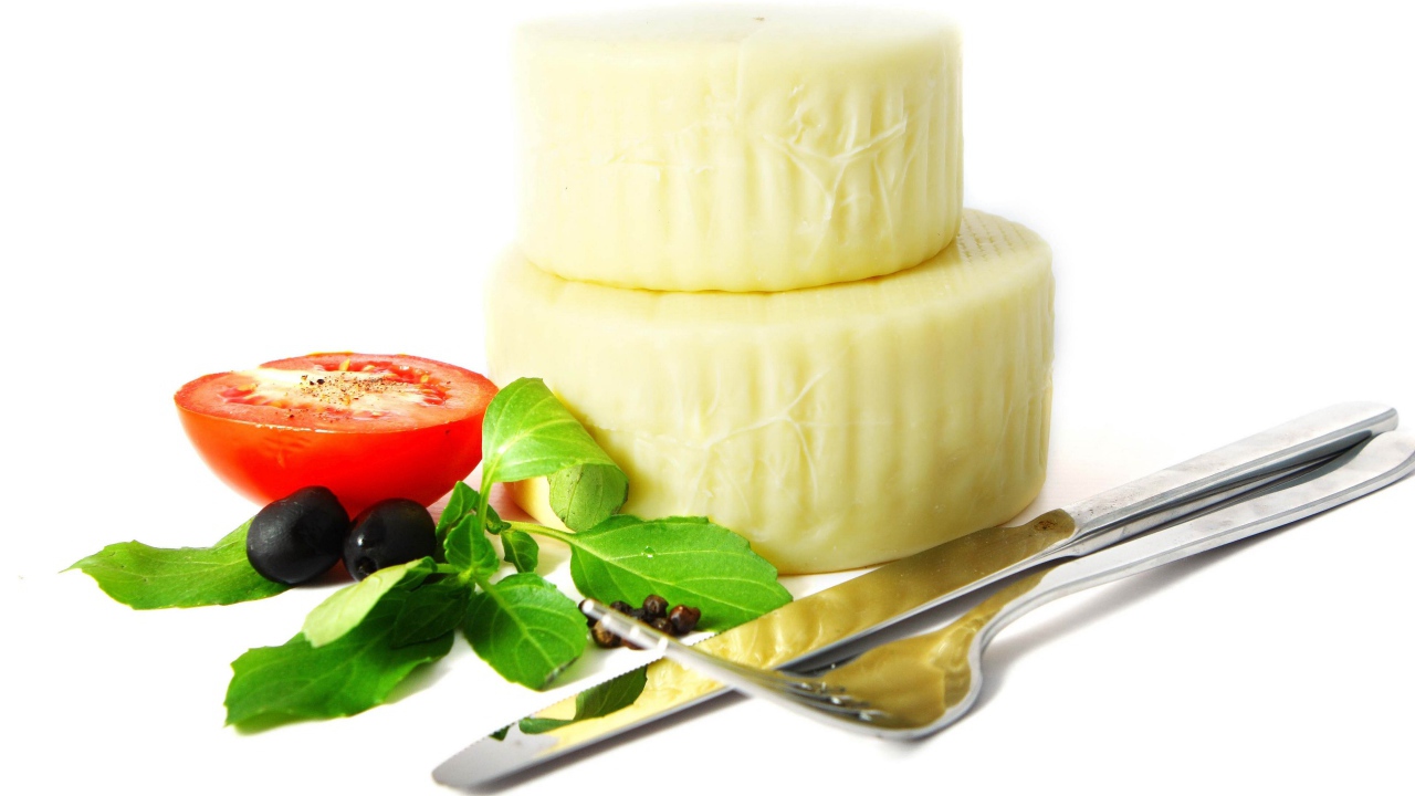 Сыр с помидором, столовыми приборами, оливками и зеленью на белом фоне
