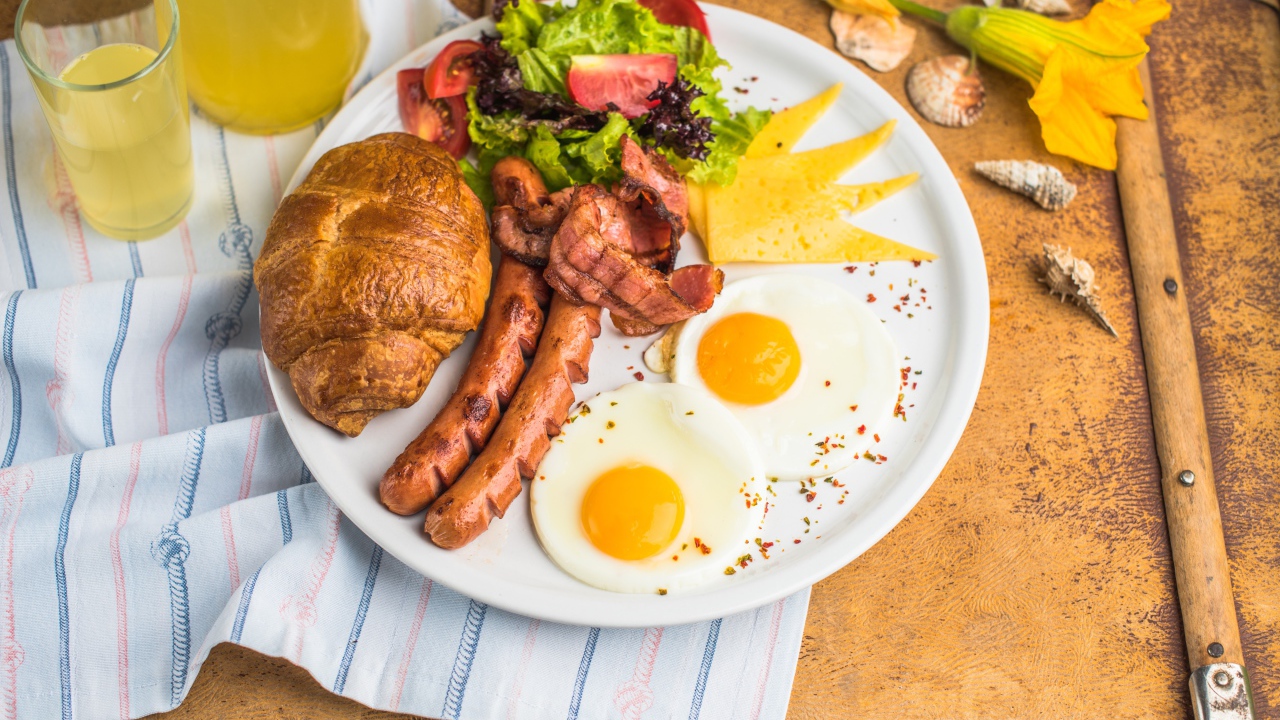 Яичница, салат, сосиски и круассан с соком на завтрак 