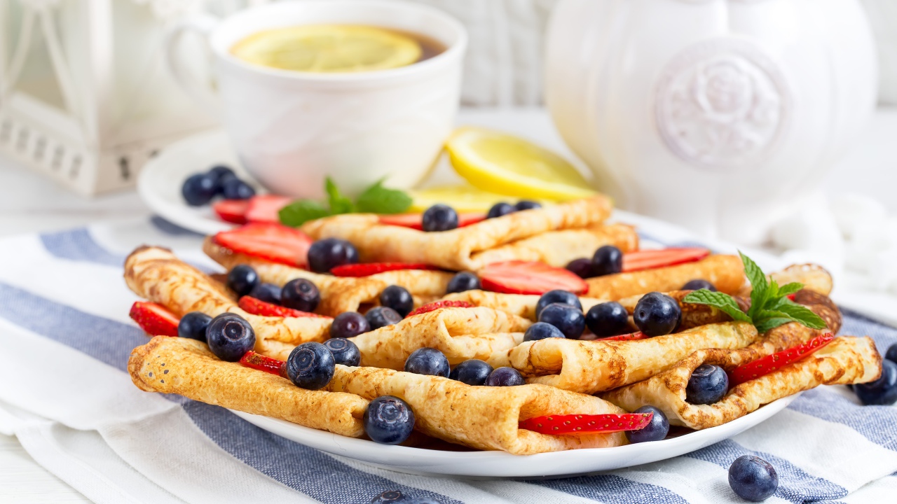 Блины с ягодами черники и клубники на столе с чашкой чаю