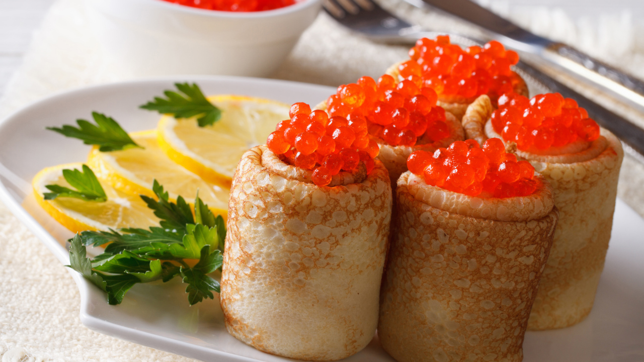 Блины с красной икрой на тарелке с лимонами и петрушкой