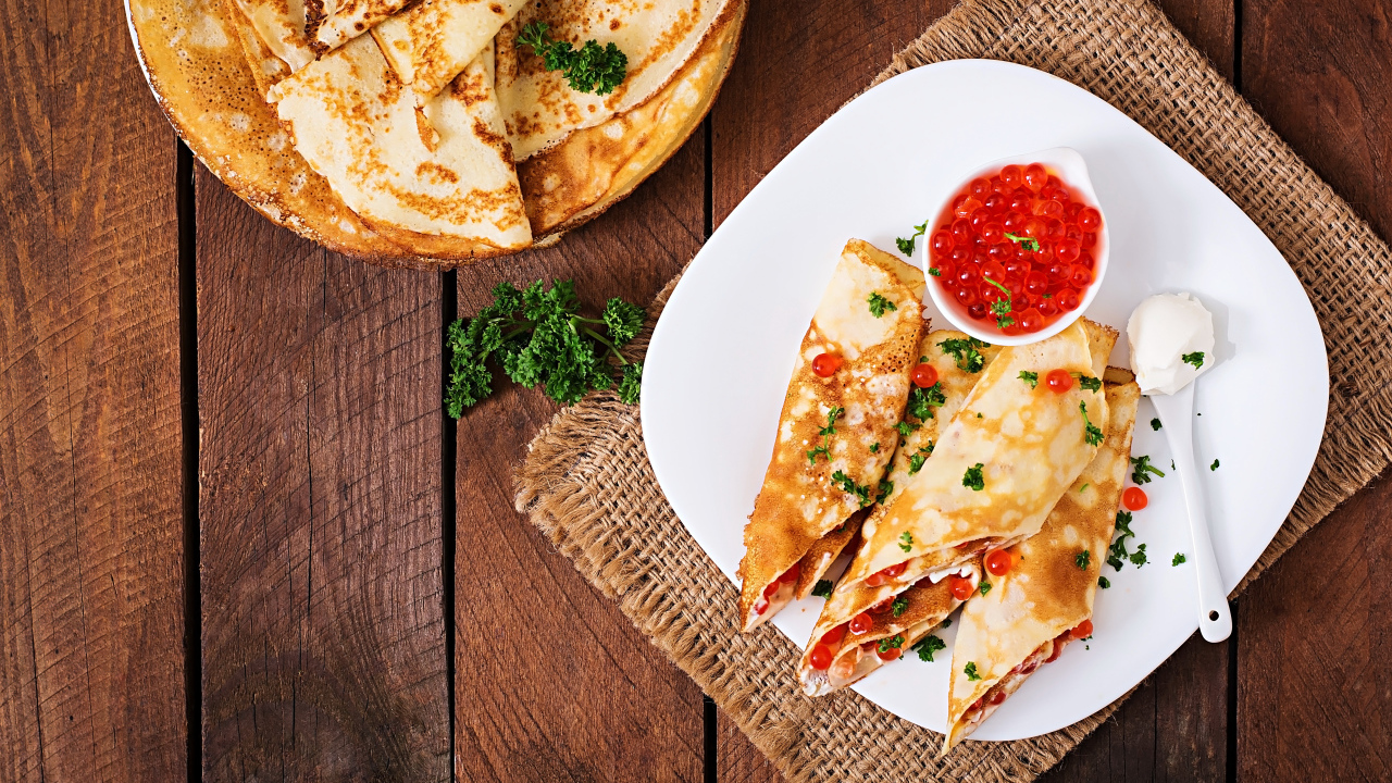 Рулетики из блинов на белой тарелке с красной икрой 