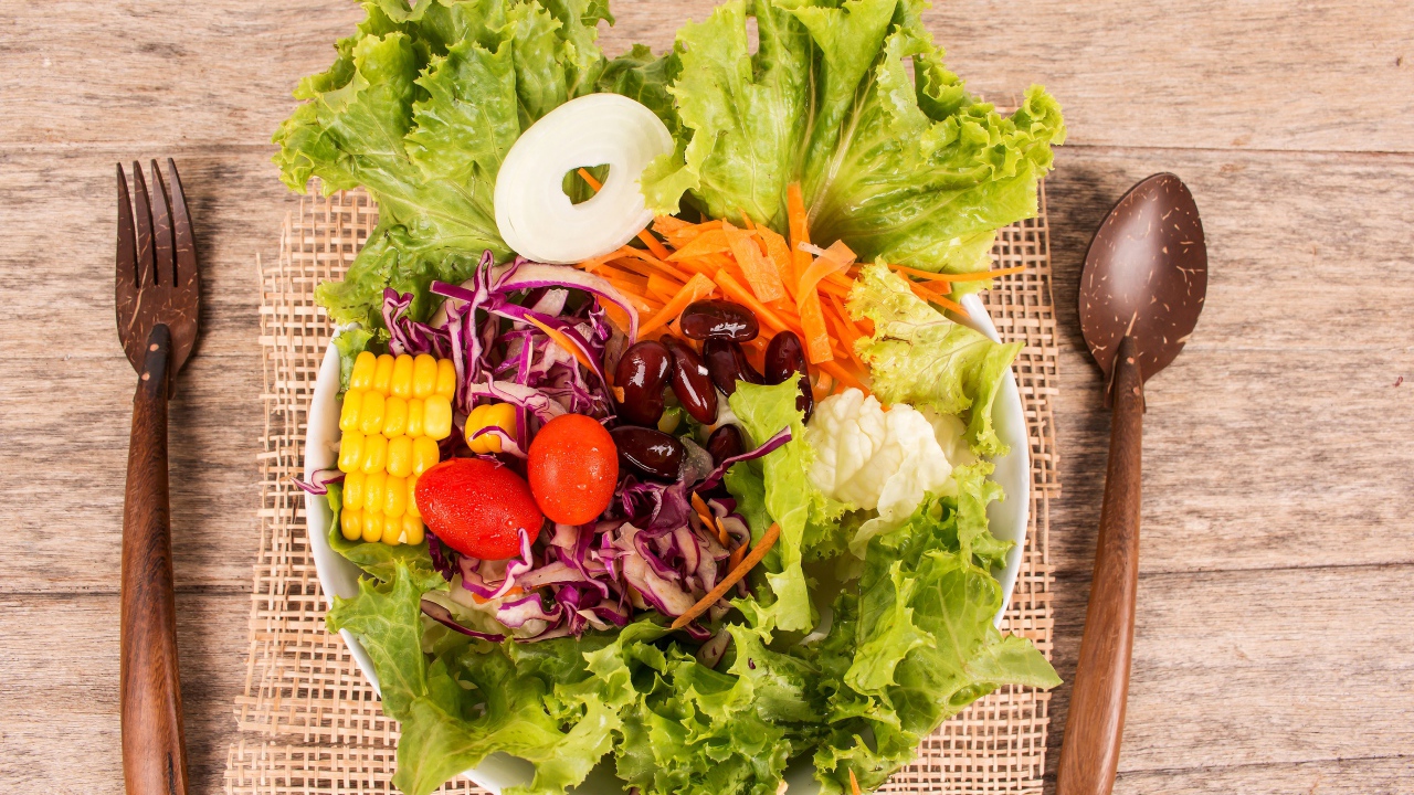 Салат с овощами и зелеными листьями салата в тарелке на столе со столовыми приборами