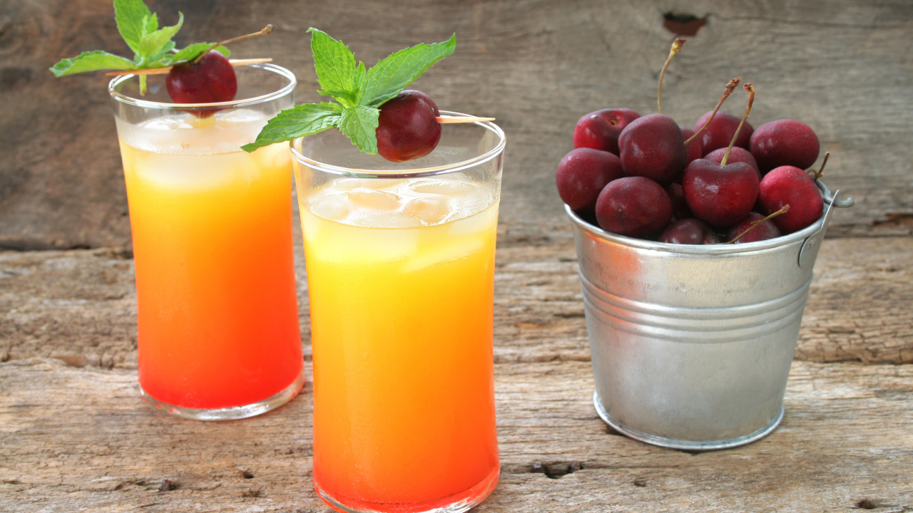Два стакана напитка на столе с ведром с черешней