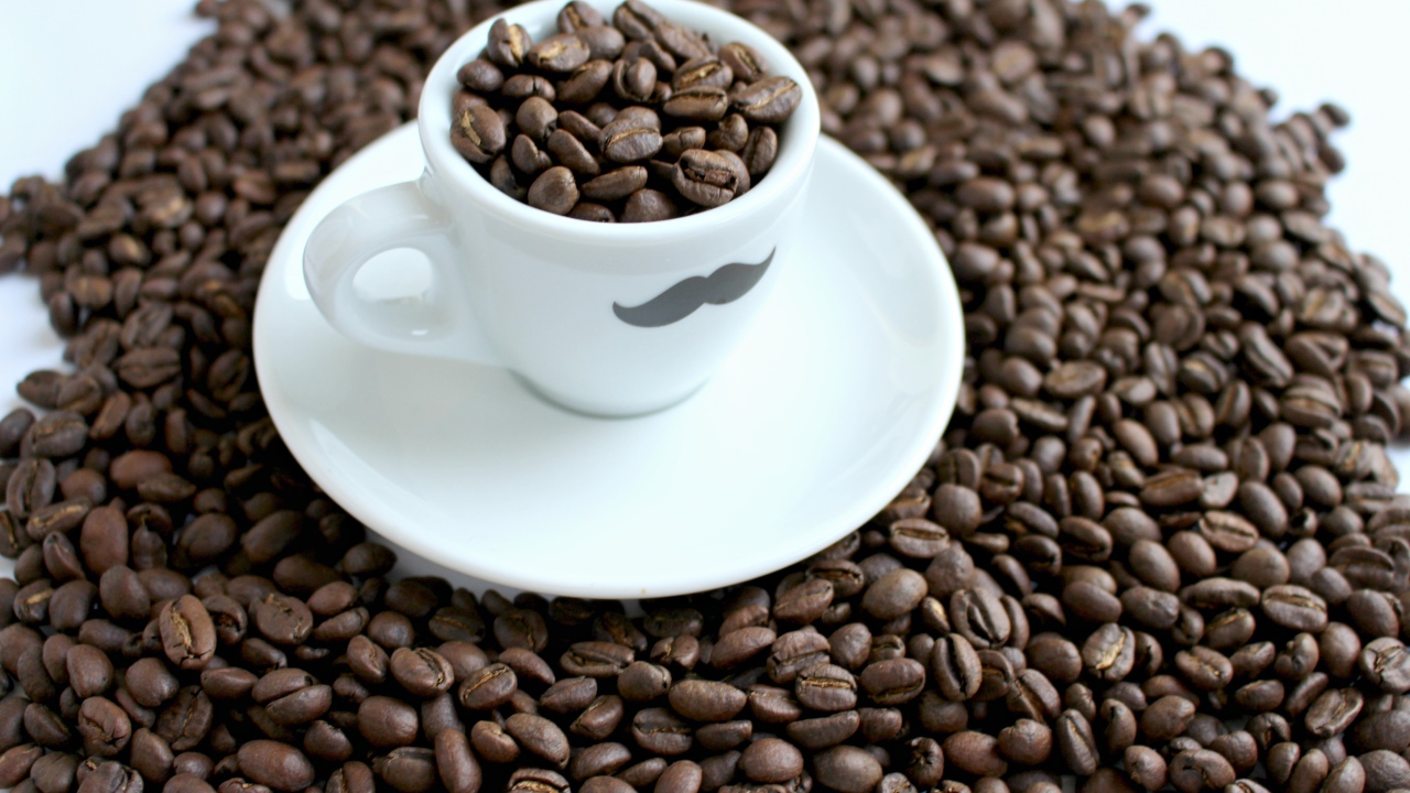 Белая чашка с жареными кофейными зернами стоит на столе с кофейными зернами