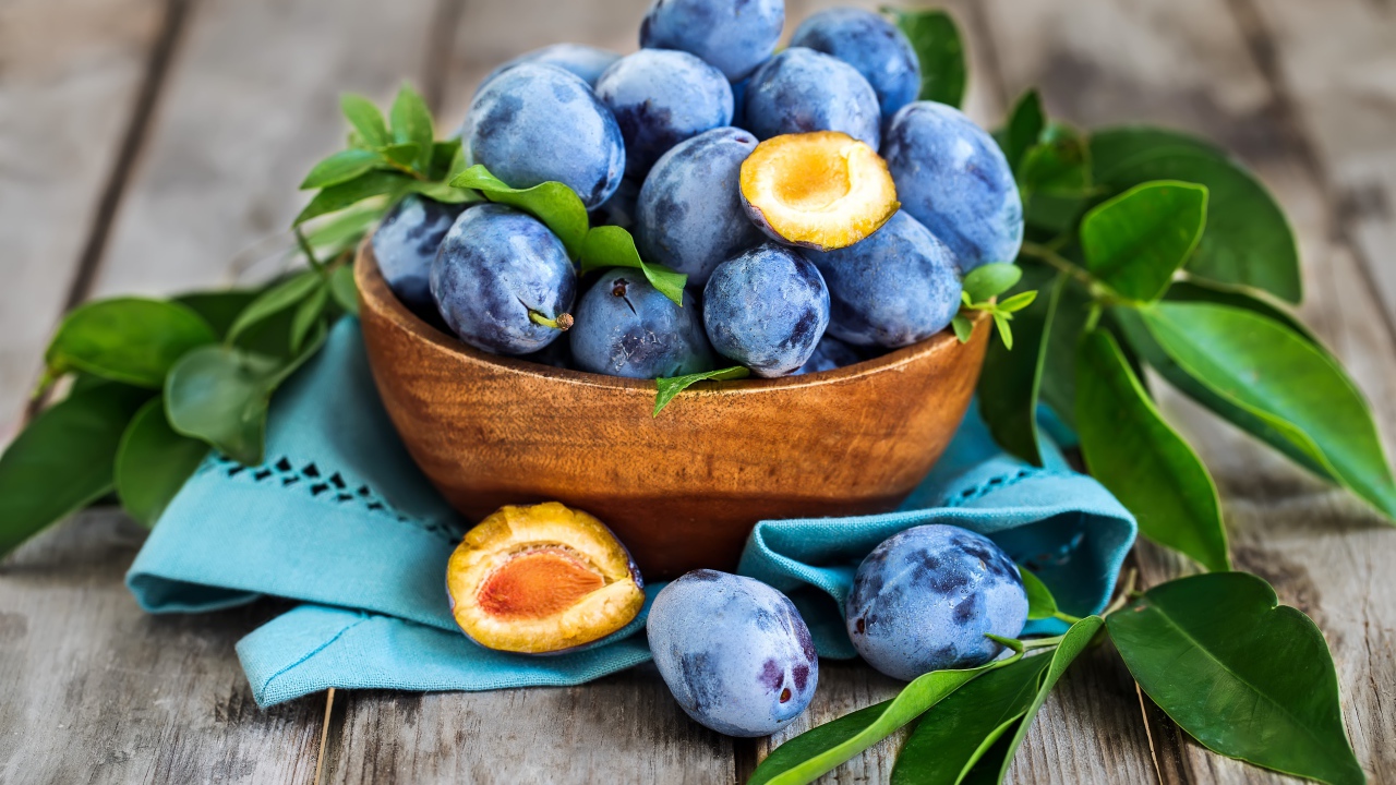 Синие сливы в деревянной миске с зеленой листвой