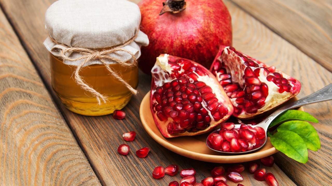 Гранат на деревянном столе с банкой меда