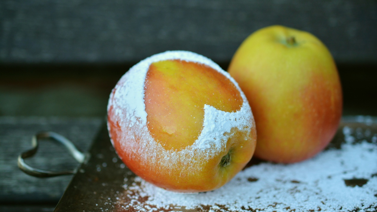 Спелое яблоко с сердцем из сахарной пудры на столе 