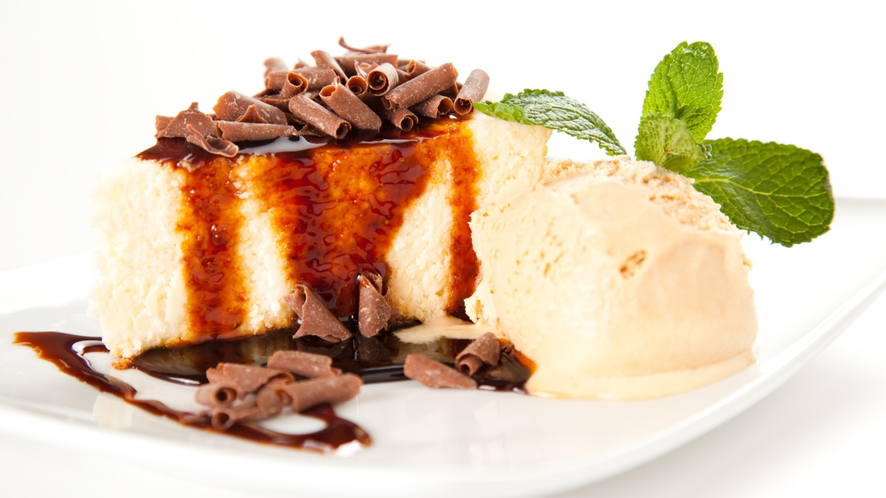 Кусок чизкейка с шоколадом и шариком мороженого на белой тарелке 