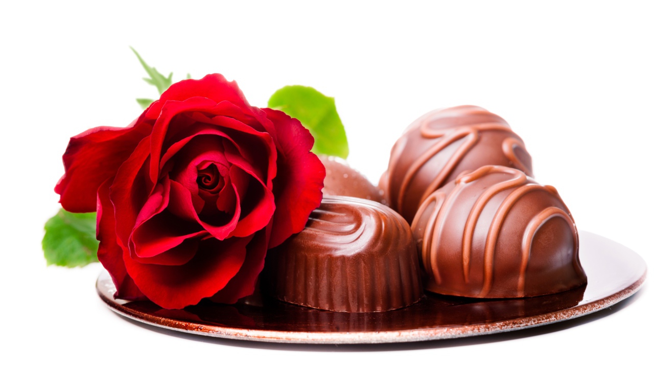 Шоколадные конфеты на тарелке с красной розой на белом фоне