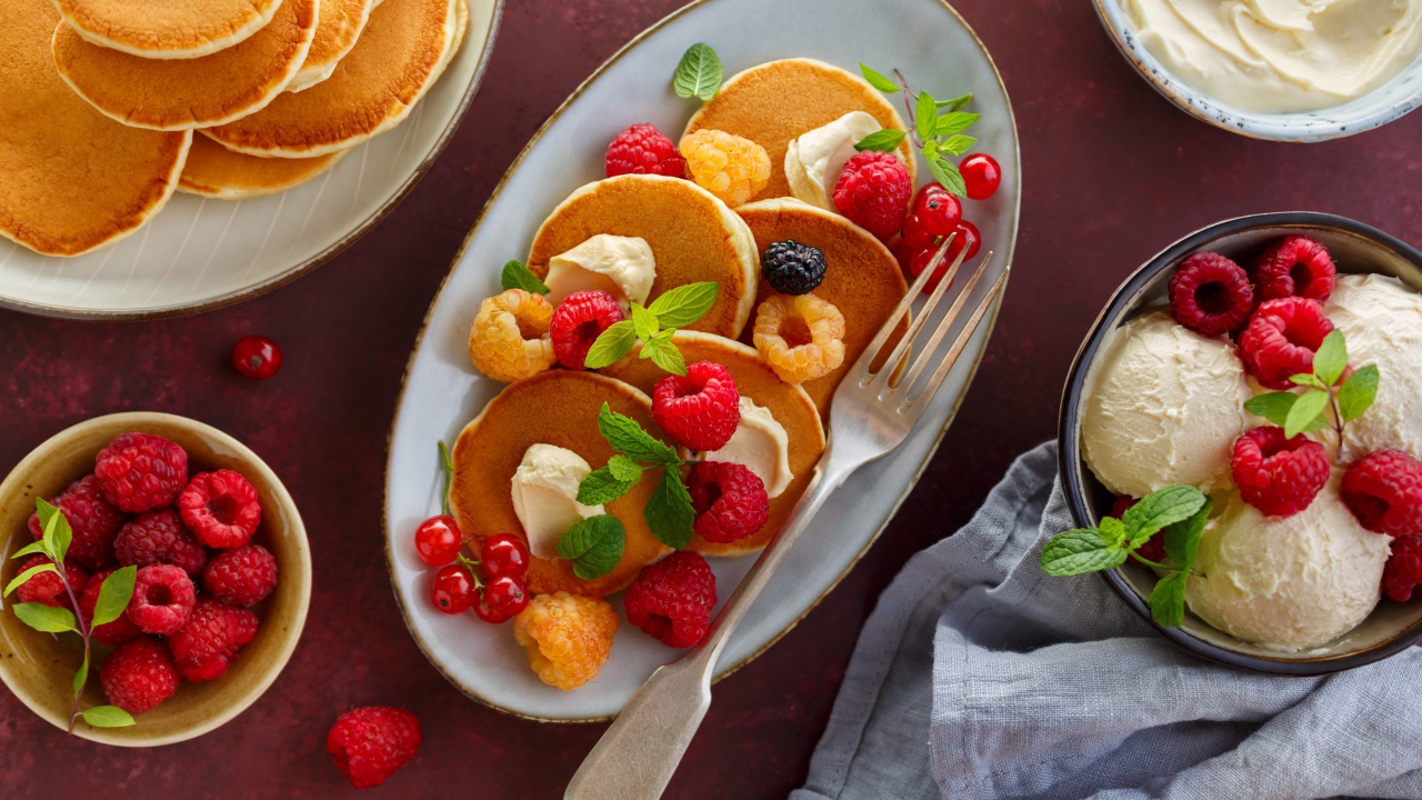 Оладьи на столе с ягодами малины и мороженым