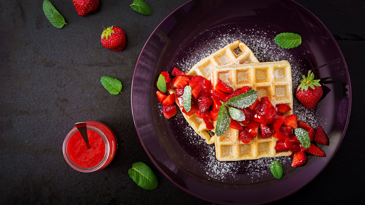 Сладкие вафли с клубникой и сахарной пудрой на тарелке 