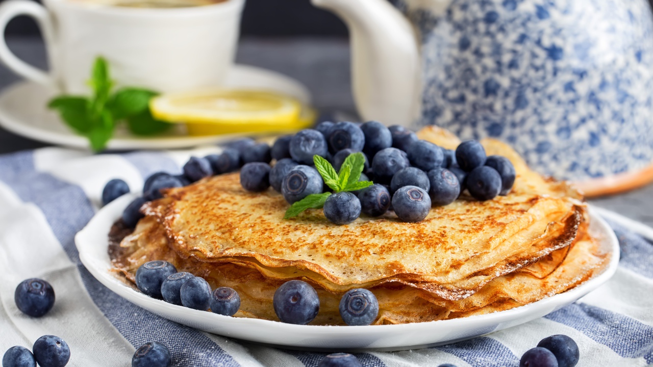 Тонкие блины с ягодами черники на столе с чаем