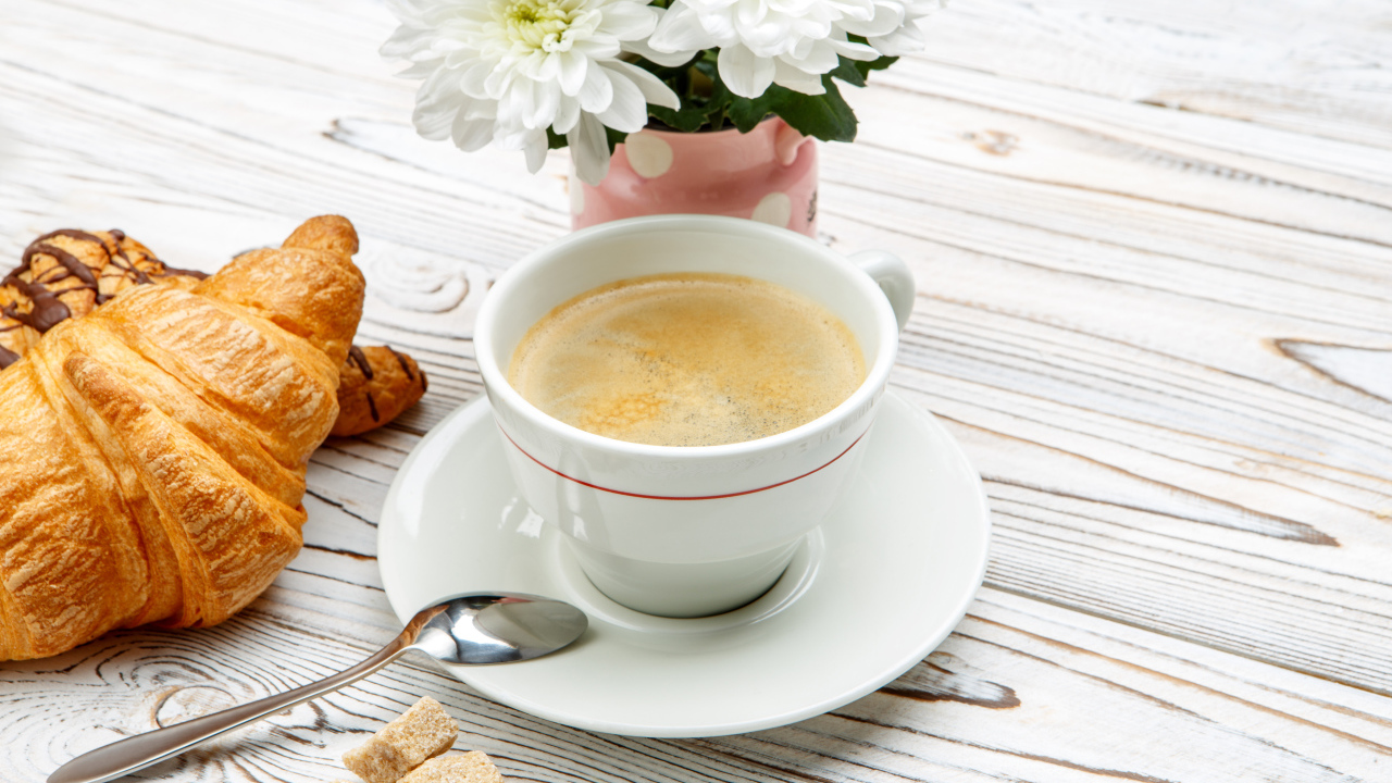 Чашка кофе и круассаны на столе с белыми хризантемами 