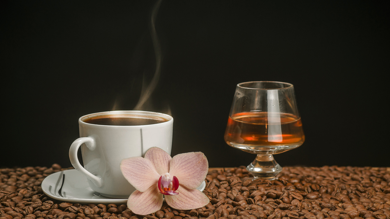 Ароматная чашка кофе на столе с бокалом виски, кофейными зернами и цветком орхидеи